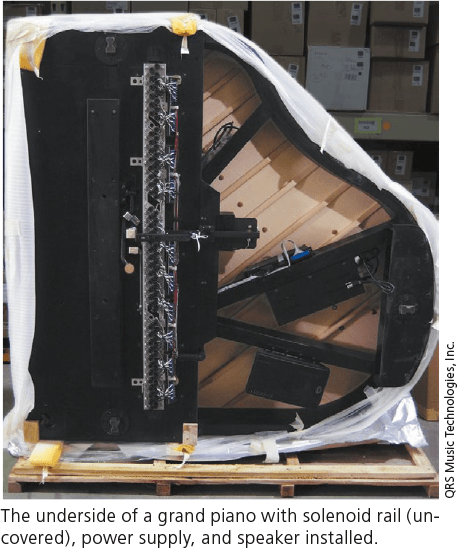 The underside of a grand piano with solenoid rail (uncovered), power supply, and speaker installed.