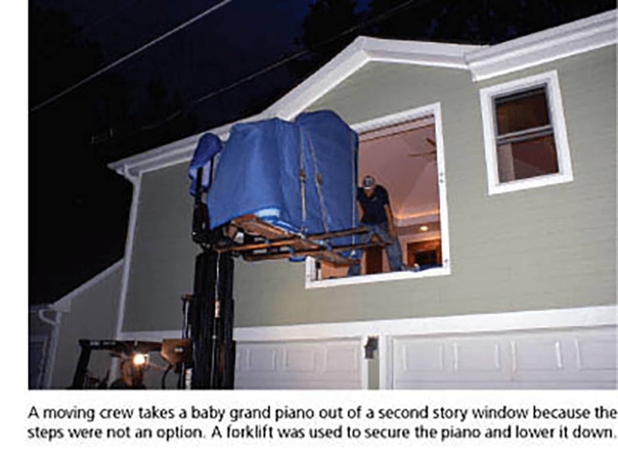 A moving crew takes a baby grand piano out of a second story window because the steps were not an option. A forklift was used to secure the piano and lower it down.